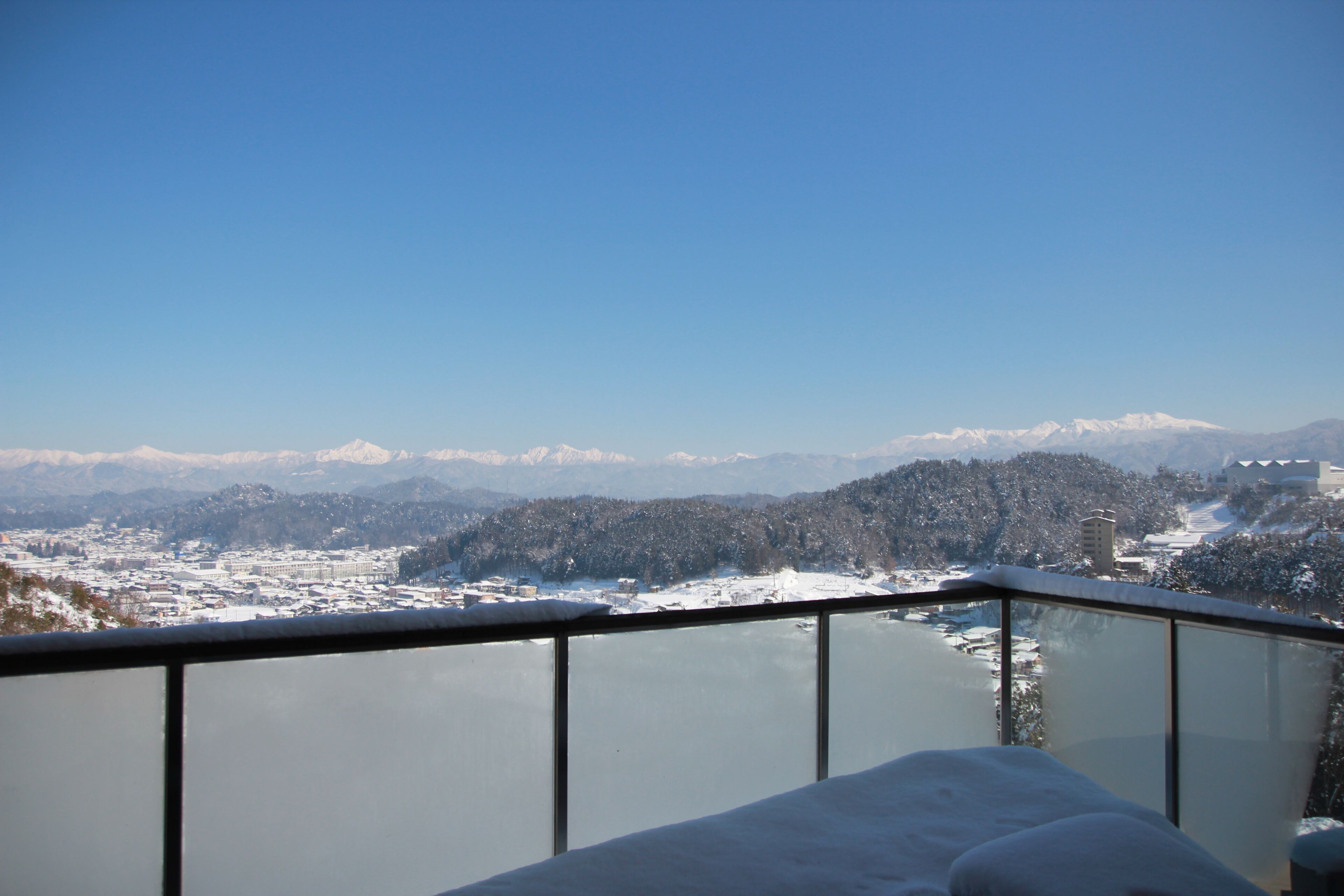 Een panoramisch uitzicht vanaf een balkon met besneeuwde bergen en een meer op de achtergrond.