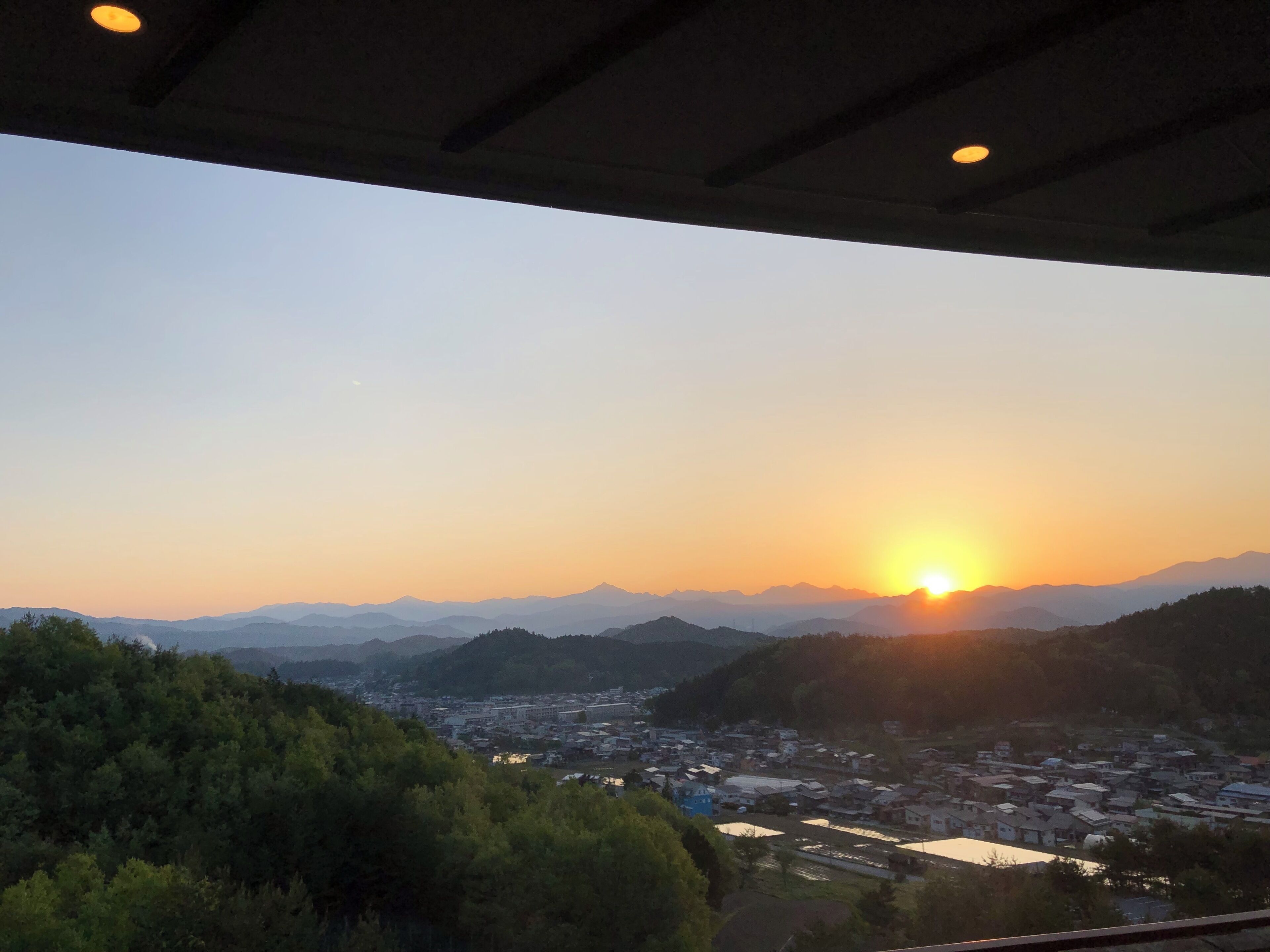 A sunset view from a covered area overlooking a town with mountains in the background.