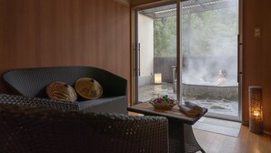 A modern room with a sofa, a table with towels, and a view of a hot spring area. - Hilton Takayama Resort (Takayama)