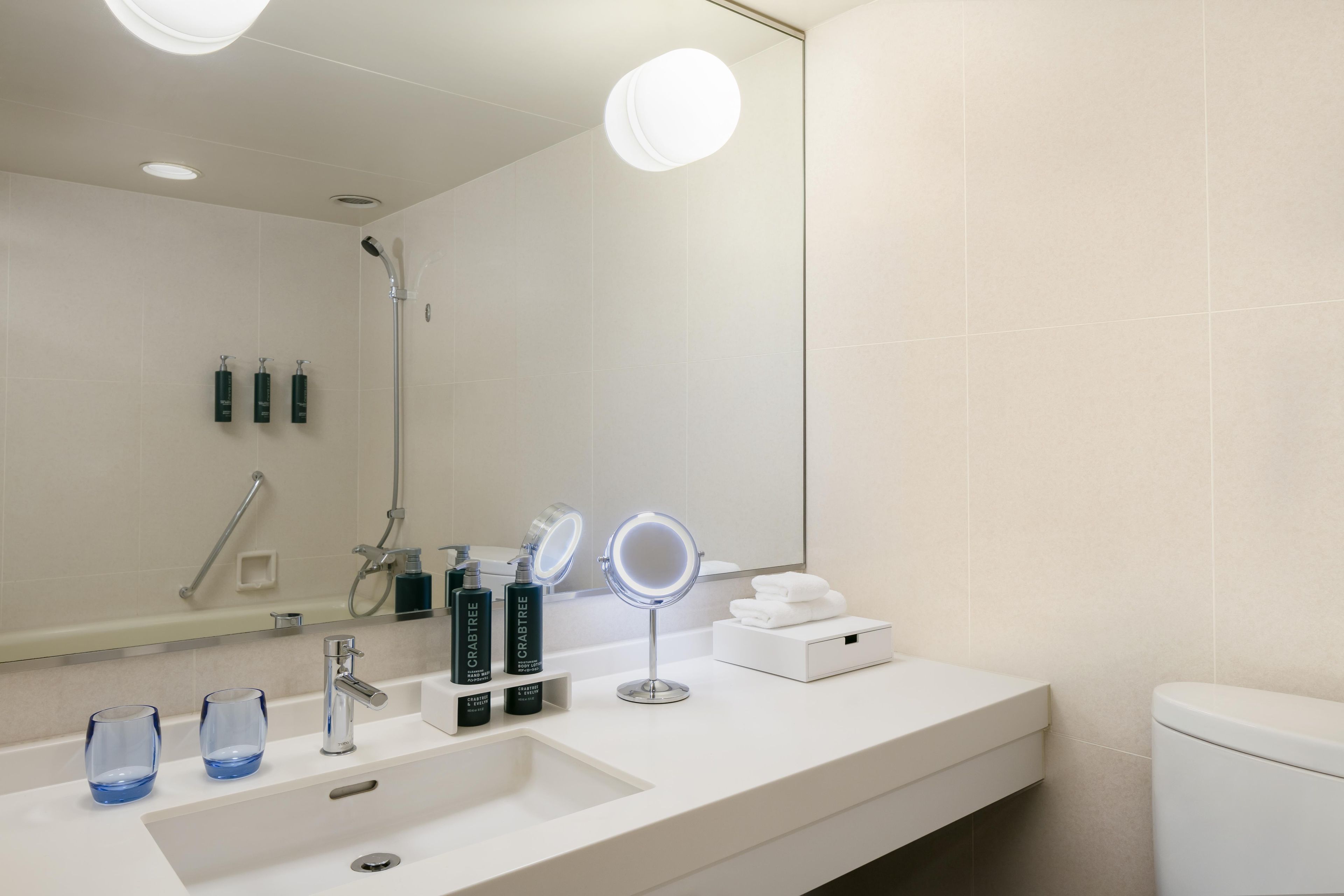 A modern bathroom with a white sink, two mirrors, and a handheld showerhead.