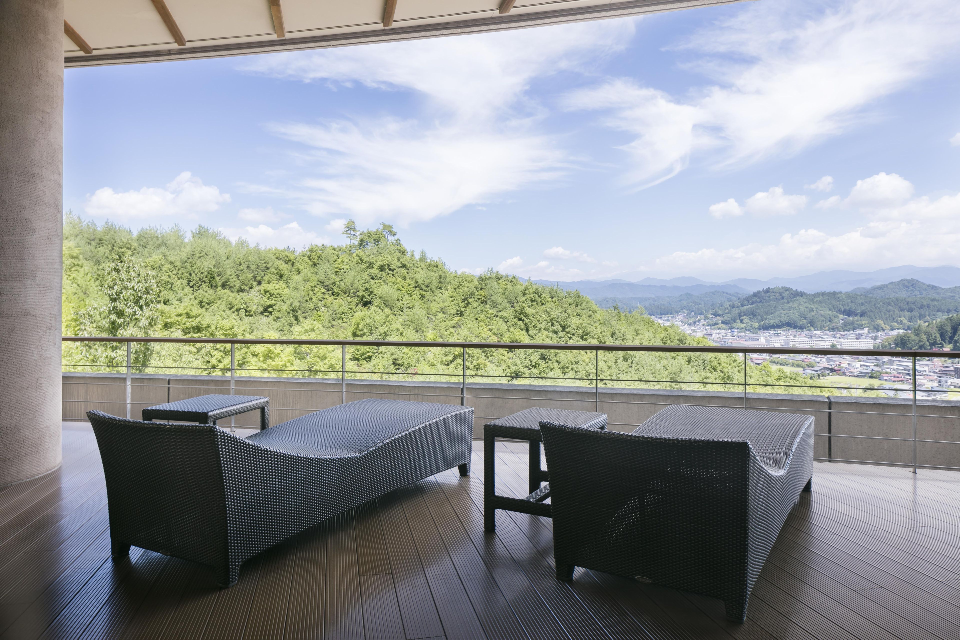 Un balcón con mobiliario de mimbre con vistas a un paisaje urbano y una colina boscosa.