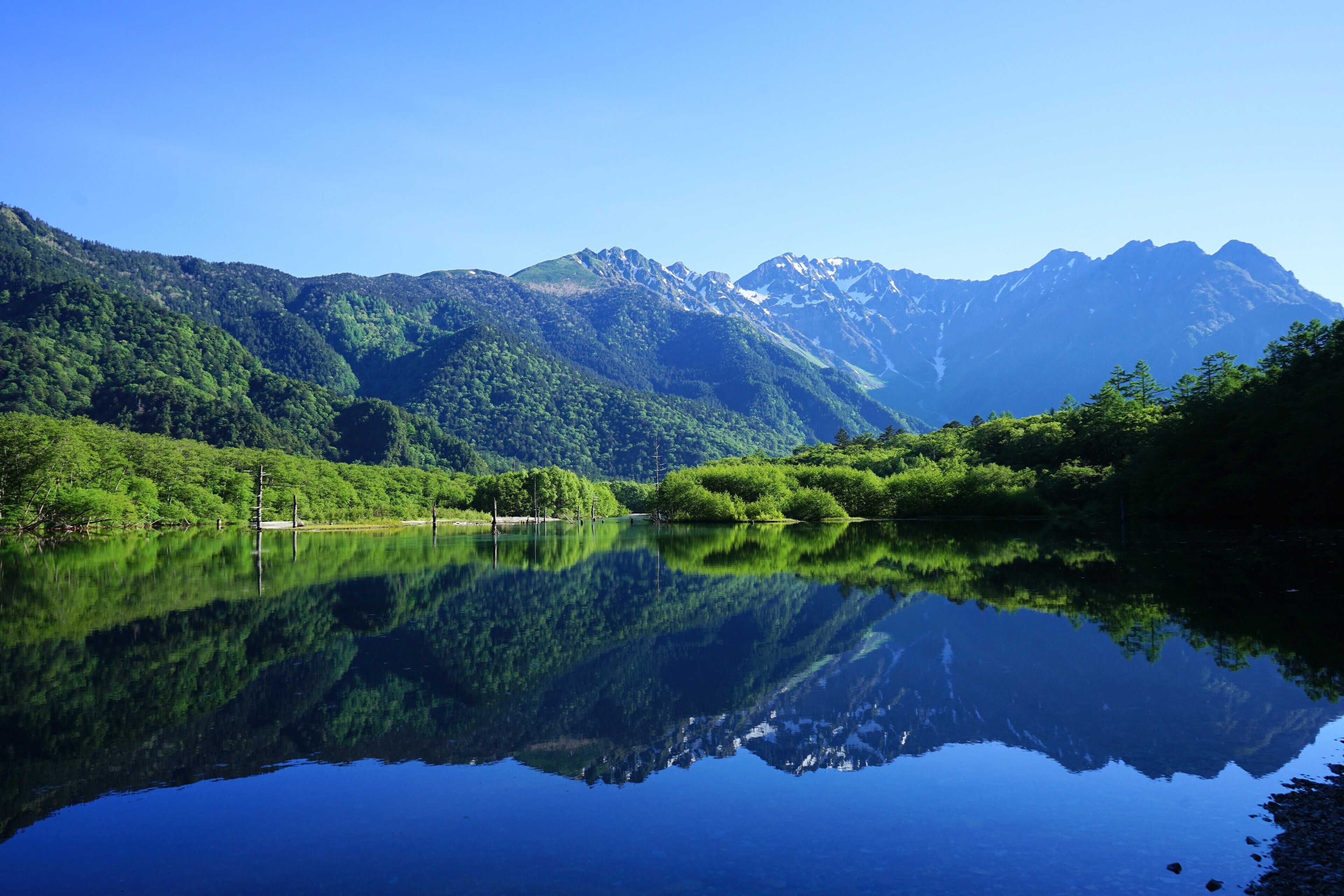A serene mountain lake with reflections of the surrounding greenery and mountains.