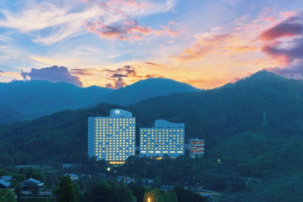 A hotel with multiple floors, surrounded by lush greenery and mountains in the background.