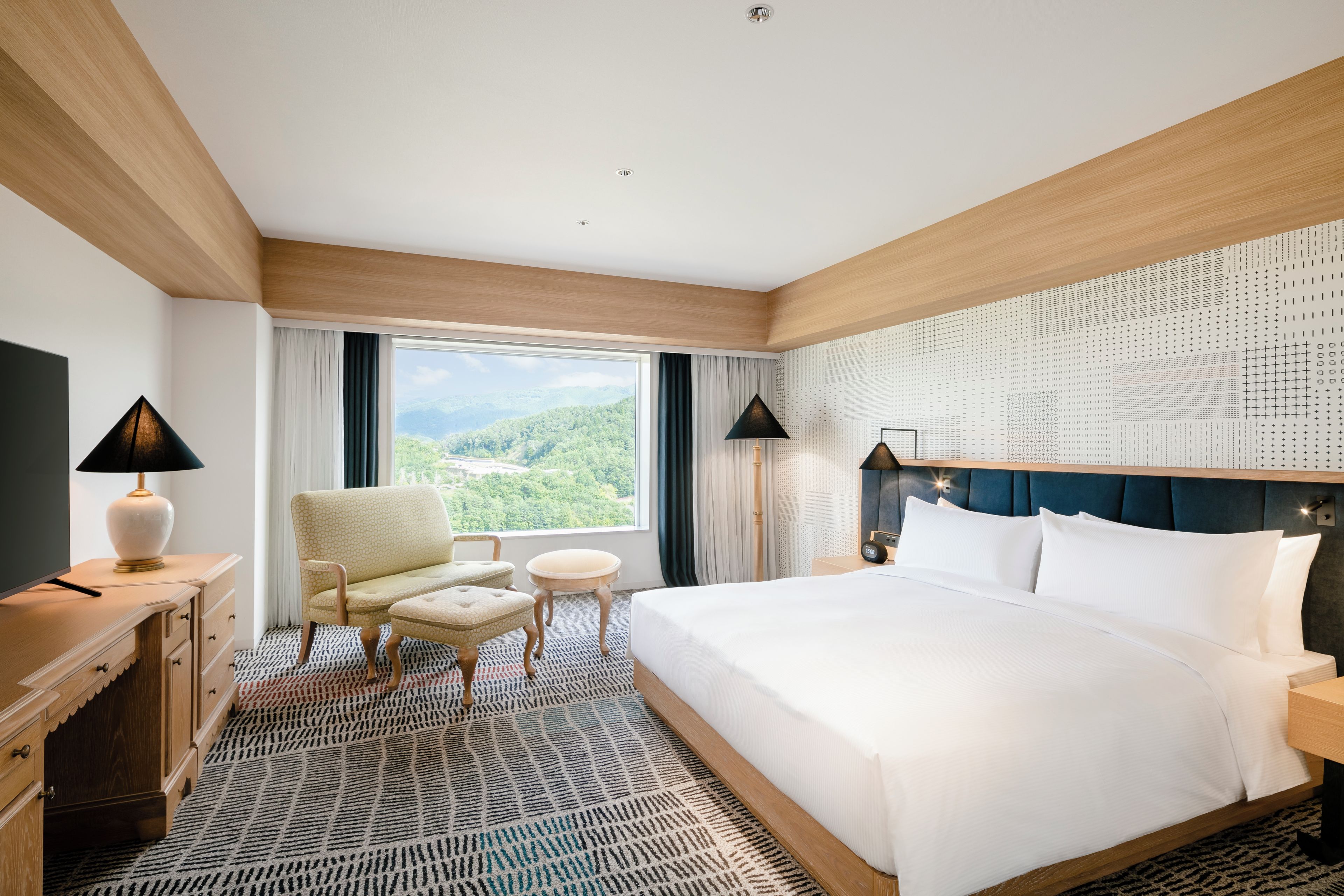 Une chambre d’hôtel avec un grand lit, une chaise, une petite table, une commode et une vue sur l’extérieur.