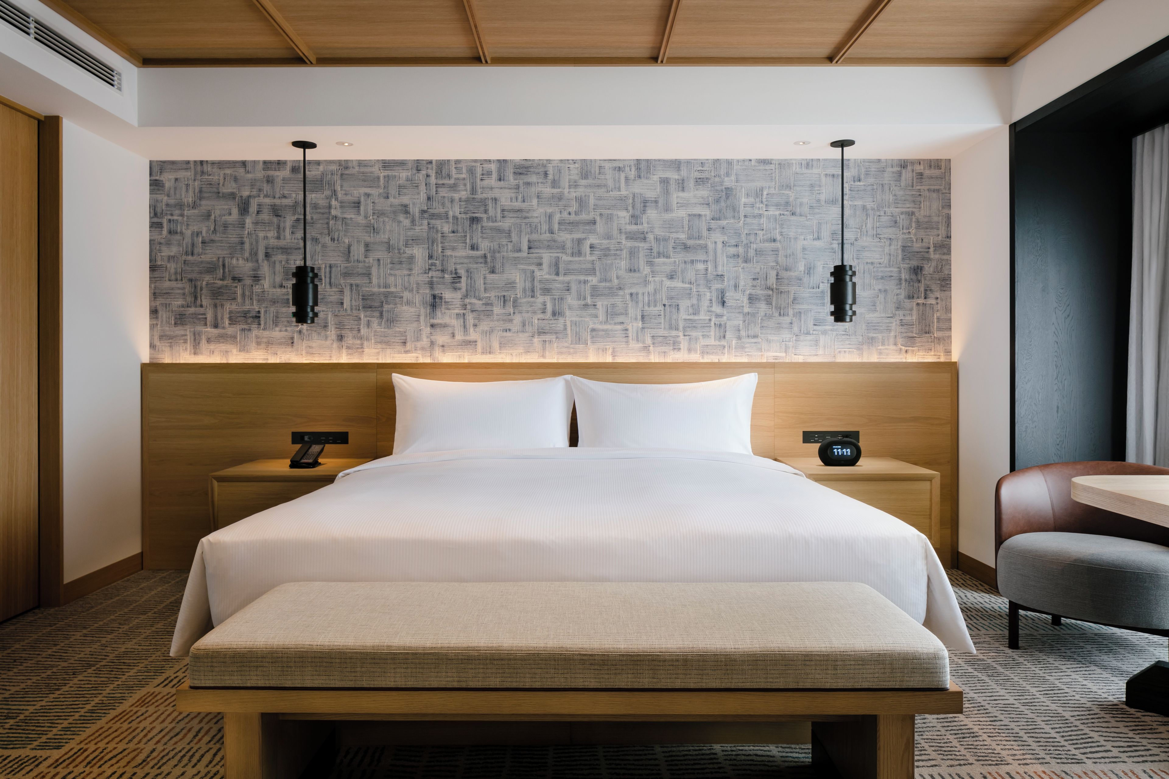 Una habitación de hotel con una cama grande, dos mesitas de noche con lámparas, un cabecero de madera y una pared con estampado.