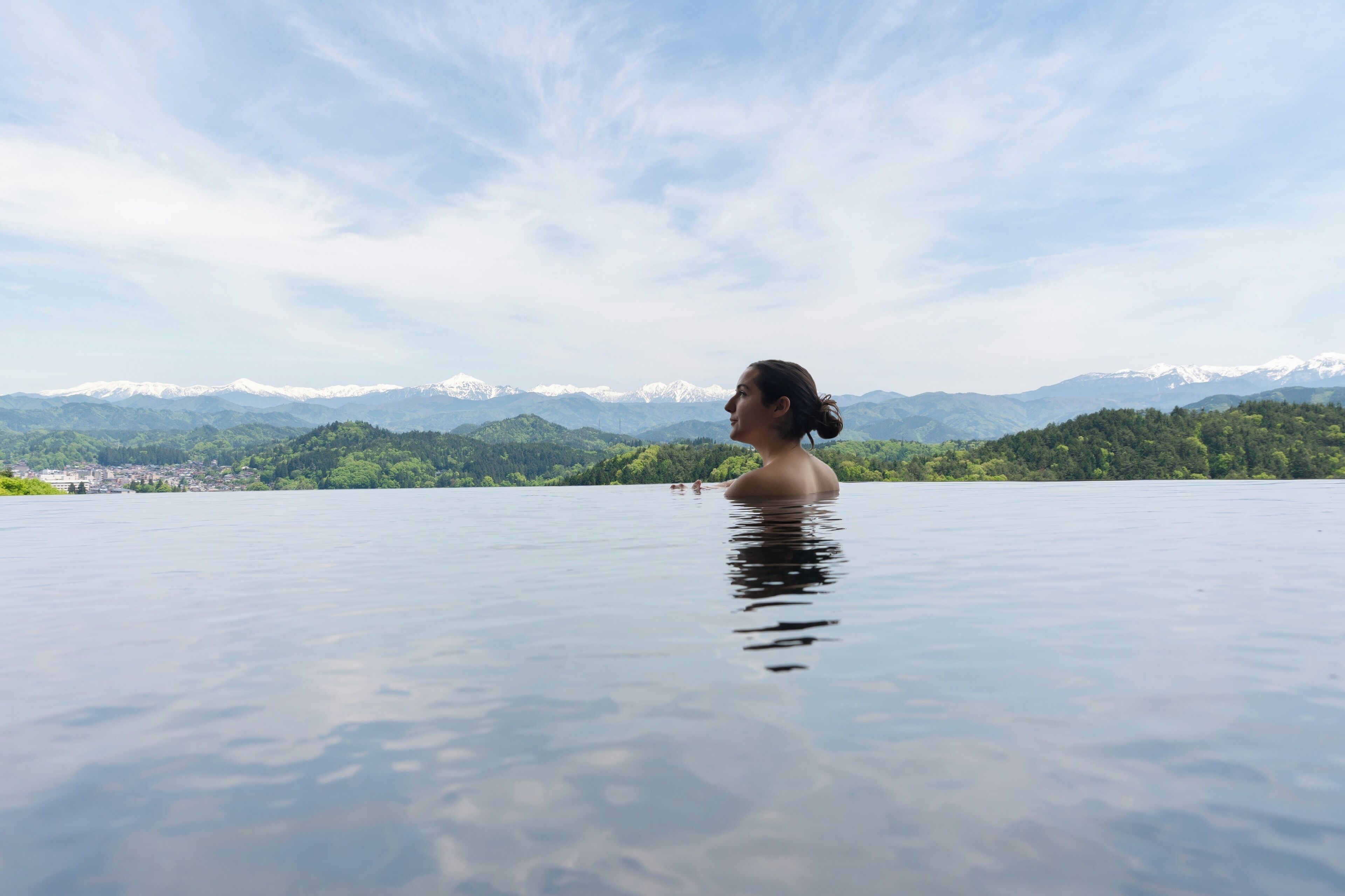 A person in a large, clear water body with a mountainous landscape in the background.