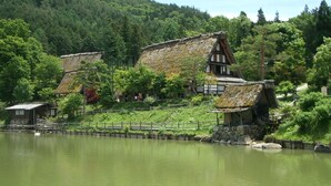 Traditionele huizen met rieten daken aan een meer, omgeven door weelderige begroeiing en heuvels.