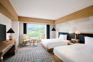 Une chambre d’hôtel avec deux lits, un bureau, une chaise, une petite table et une vue sur un paysage montagneux.