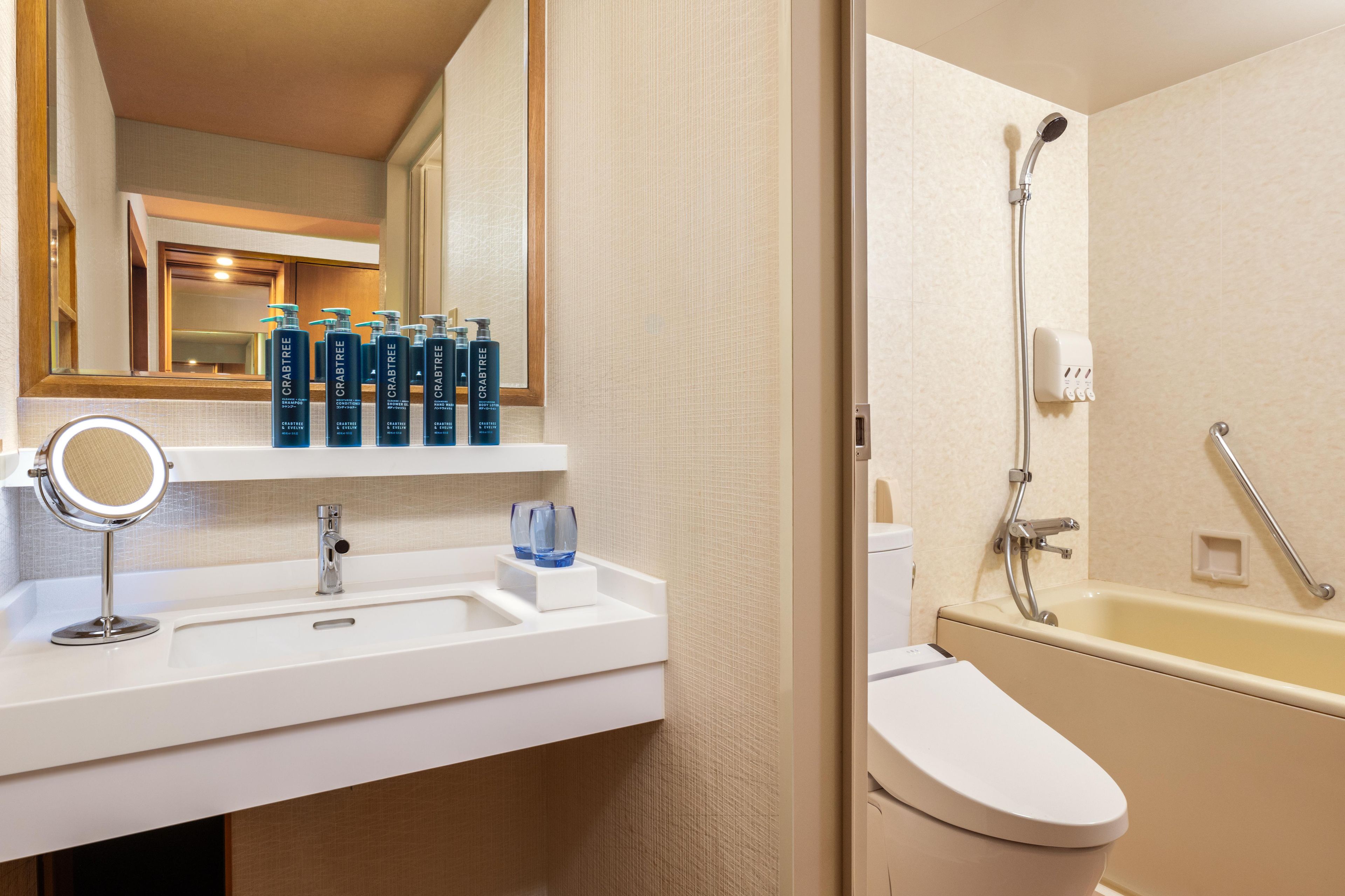 A bathroom with a white sink, a mirror, and a shower. There are bottles of Crabtree body lotion on the sink.