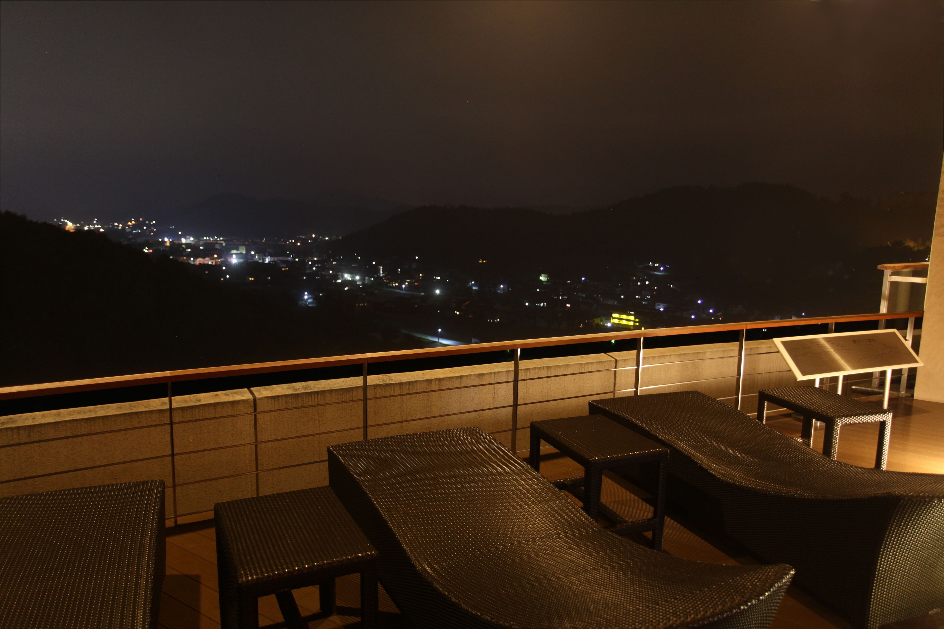 Un balcón con mobiliario de mimbre y vista a la ciudad por la noche.