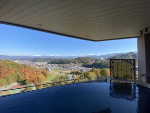 A view from a balcony with a pool, overlooking a town and mountains.