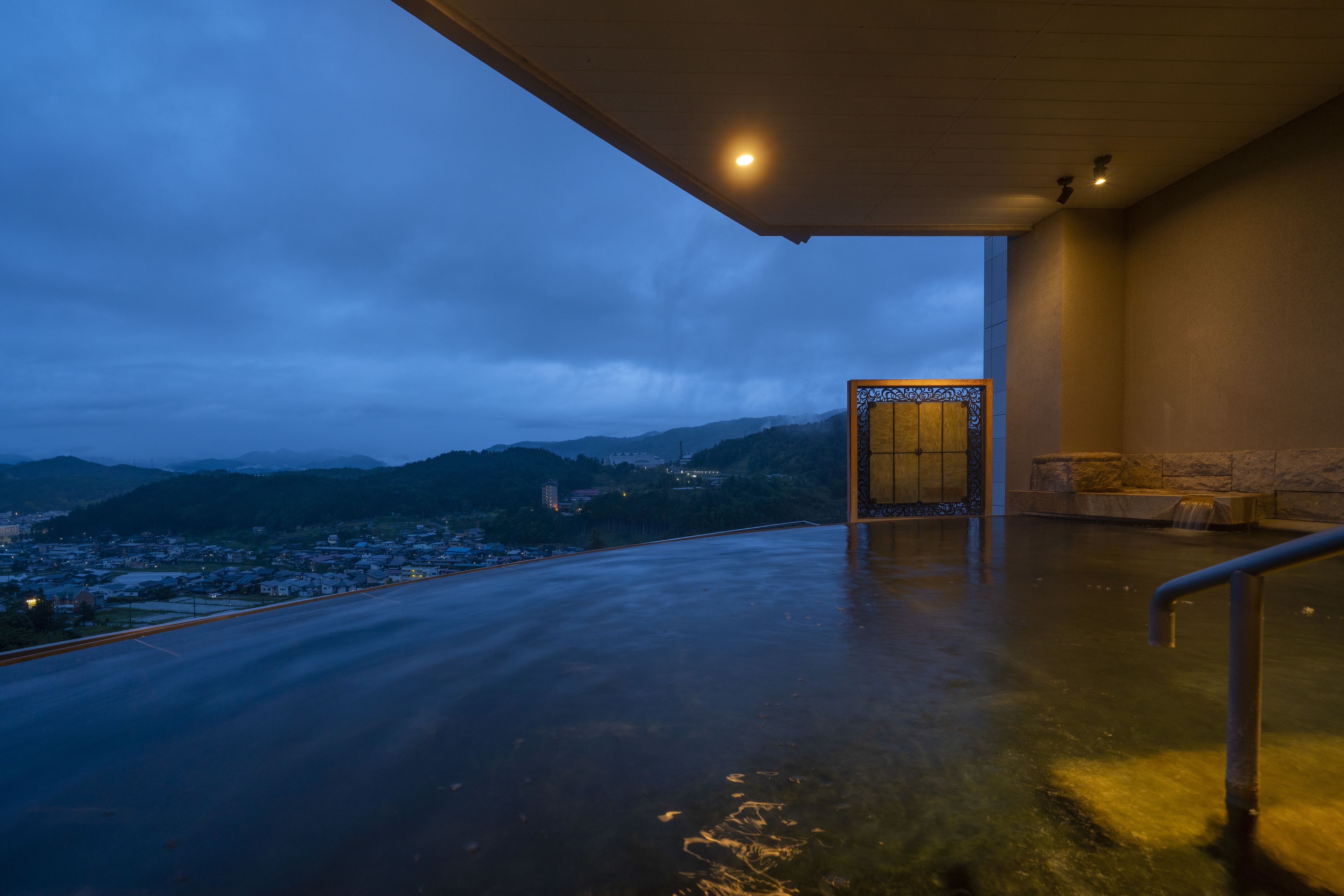 A modern building with a large glass entrance, a view of a city and mountains in the background, and a wet floor indicating recent rain.