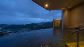 A modern building with a large glass entrance, a view of a city and mountains in the background, and a wet floor indicating recent rain.