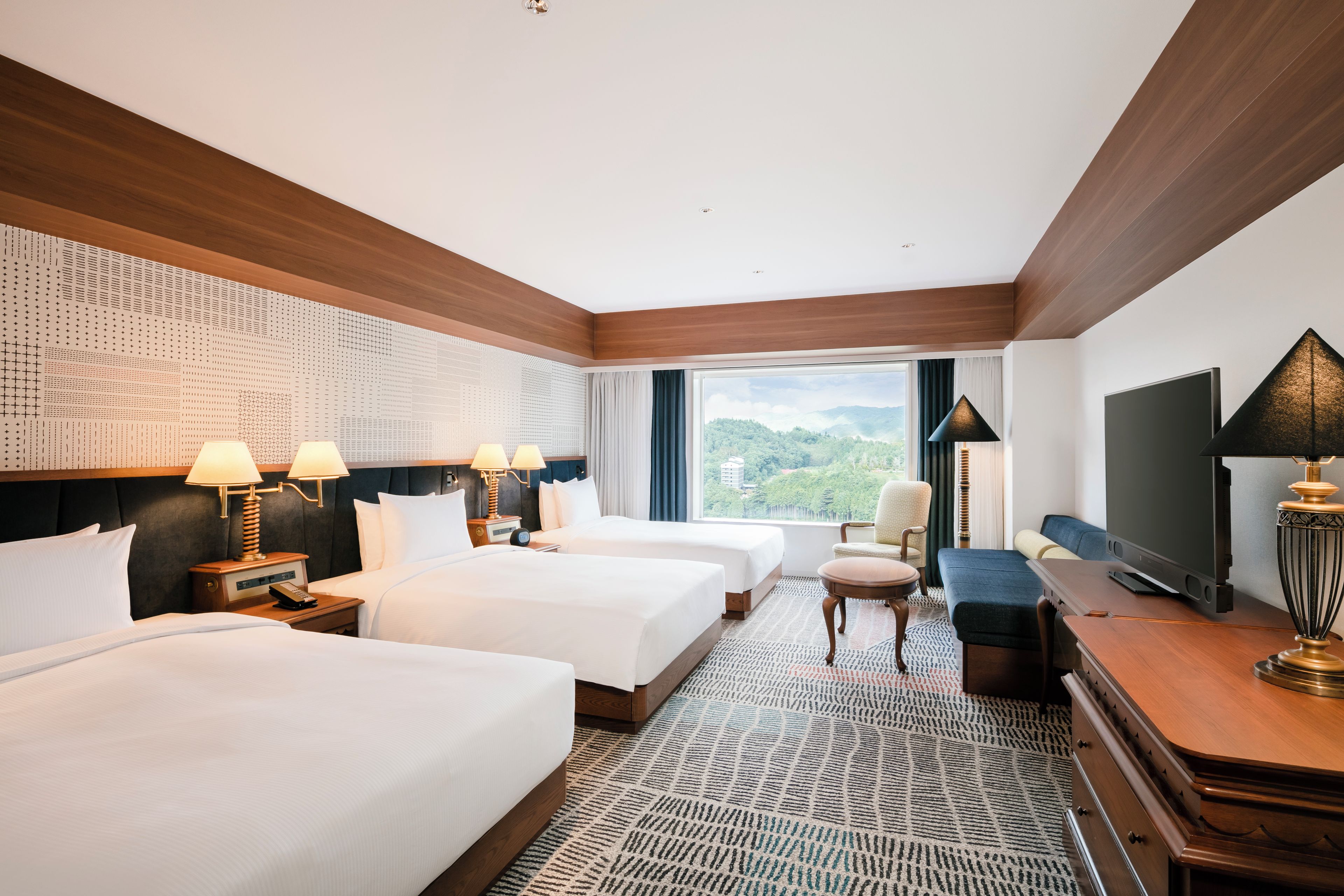 Habitación de hotel con dos camas, un televisor, un escritorio y vistas a un paisaje montañoso.