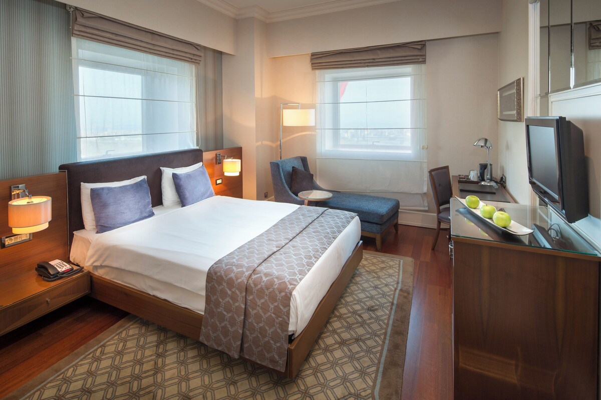 A hotel room with a large bed, bedside lamps, a desk with a television, and a chair.