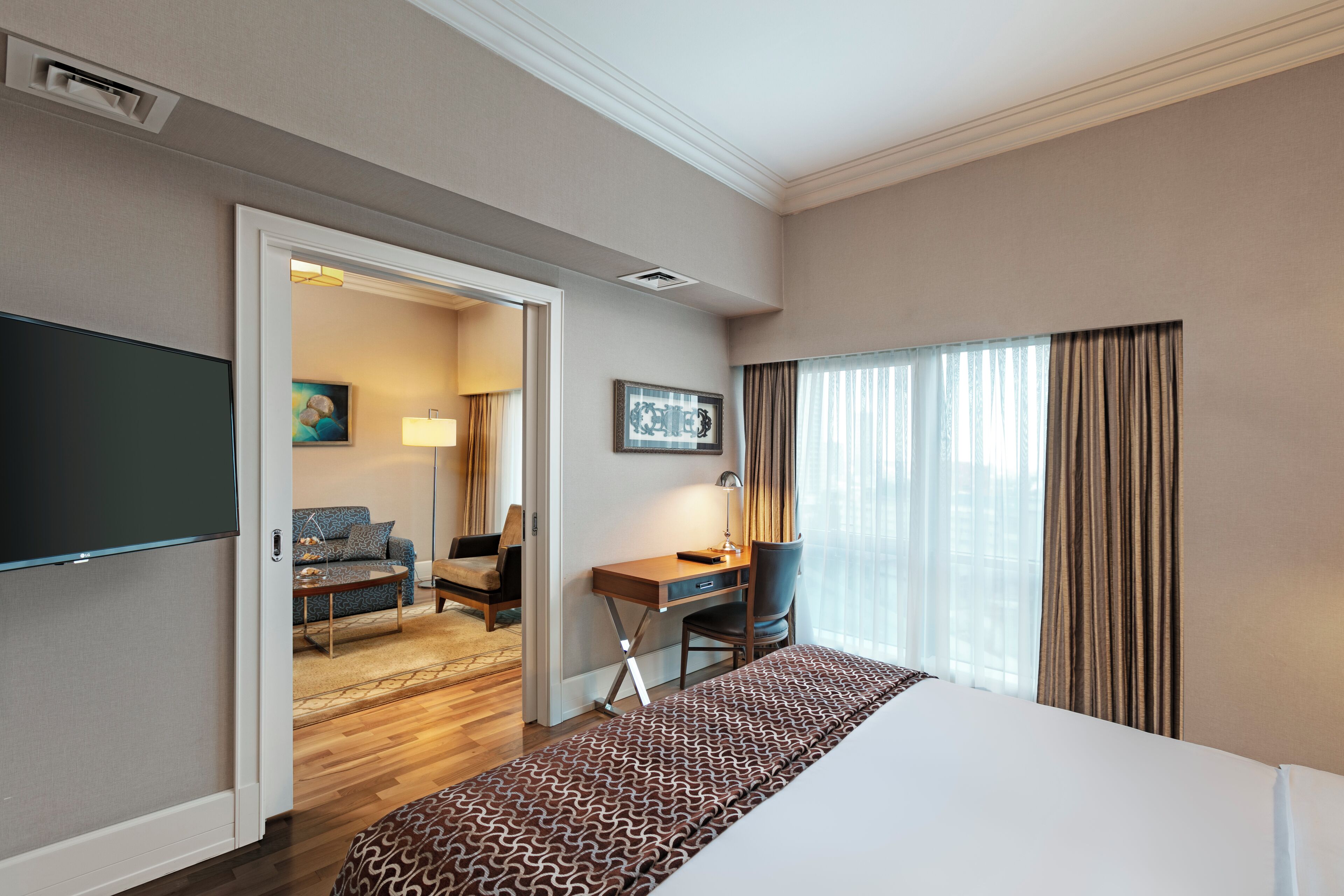 A hotel room with a large bed, a desk with a chair, a television, and a view of the outdoors through a window.