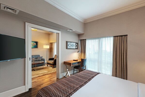 Habitación de hotel con una cama grande, un escritorio con una silla, televisión y vistas al exterior a través de una ventana.