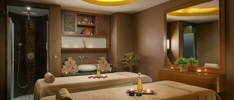 A spa room with two beds, a shower area, and a vanity with a mirror.