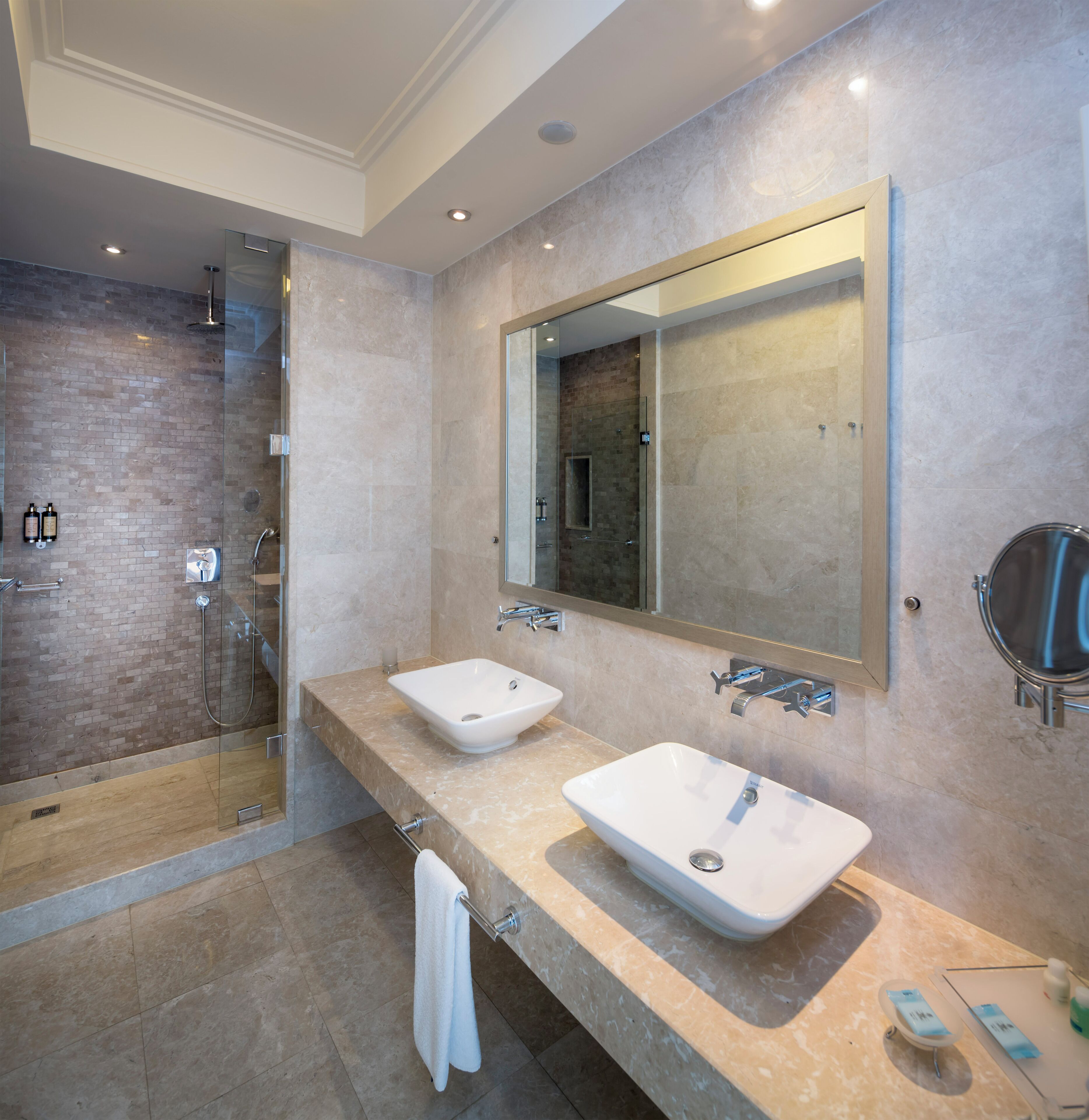 A modern bathroom with two sinks, a glass shower enclosure, and a large mirror.