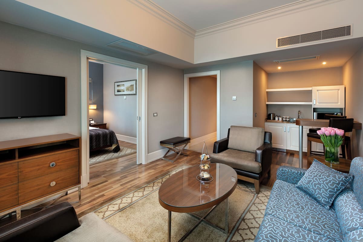 A modern living room with a flat-screen TV, a sofa, a coffee table, and a dining area with a kitchen in the background.