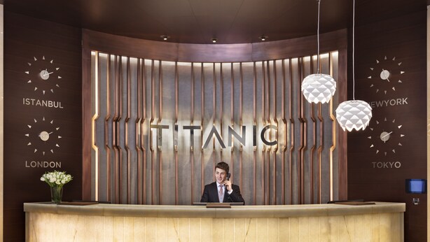 A reception desk with a large sign reading "TITANIC" and clocks indicating "ISTANBUL," "LONDON," and "TOKYO." - Titanic Business Kartal (Istanbul)