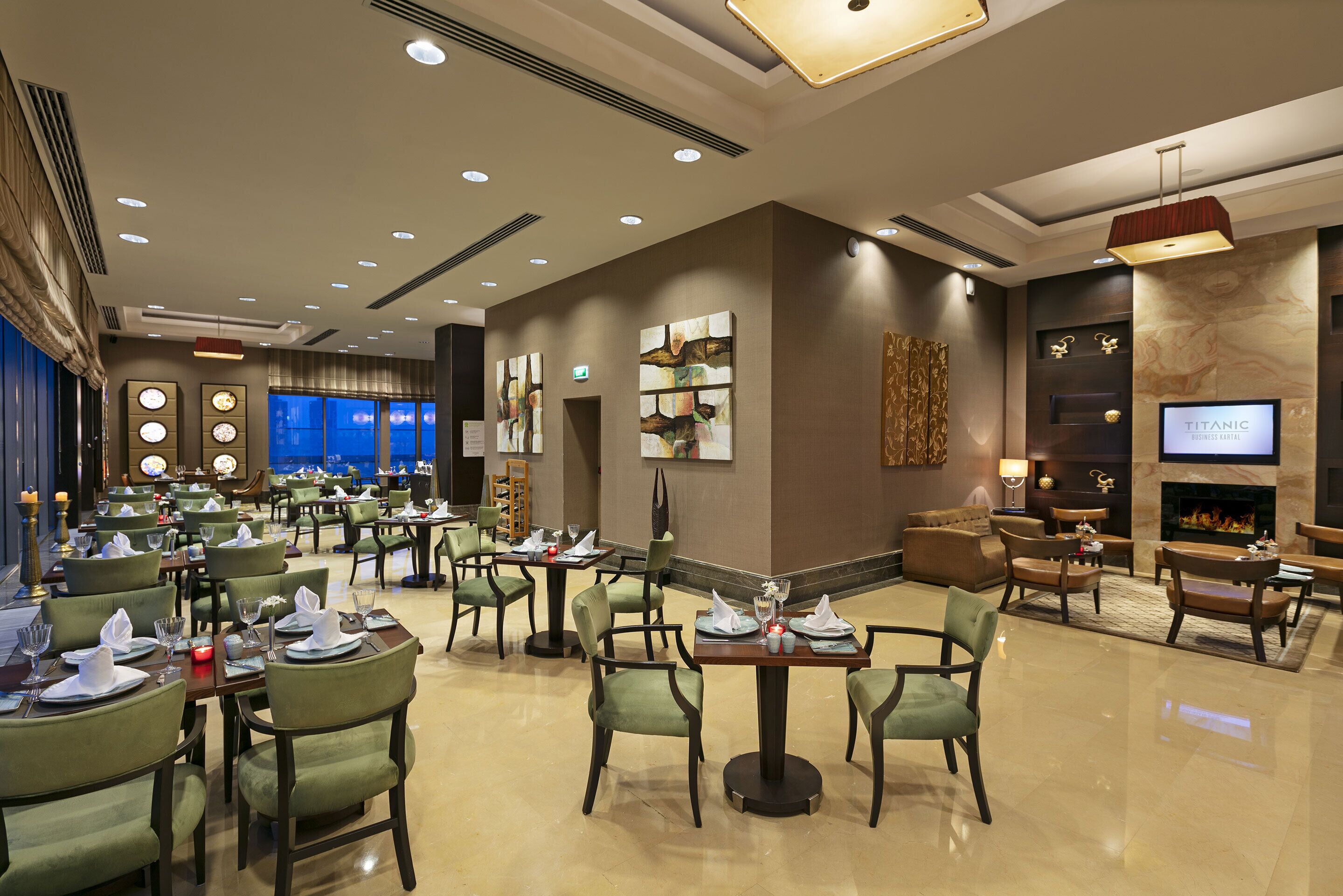 Een ruime hotel lobby met meerdere eettafels, comfortabele zithoeken, een open haard en een televisiescherm.