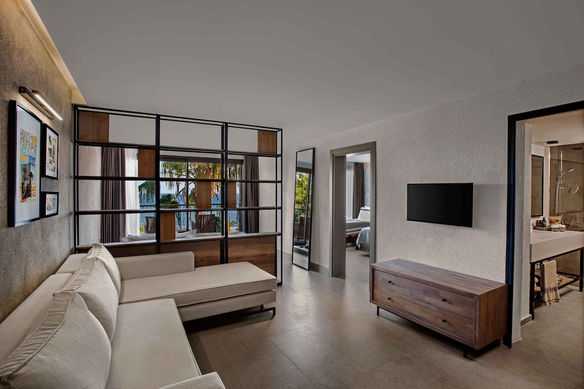 A modern living room with a sectional sofa, a wooden cabinet, a flat-screen TV, and a large window with a view of greenery.