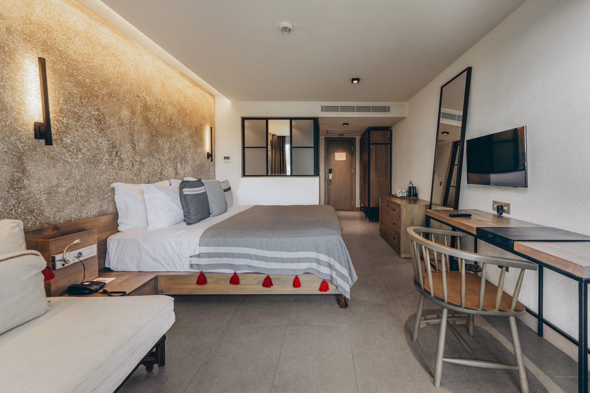 A modern hotel room with a bed, bedside table, desk, chair, and a television.