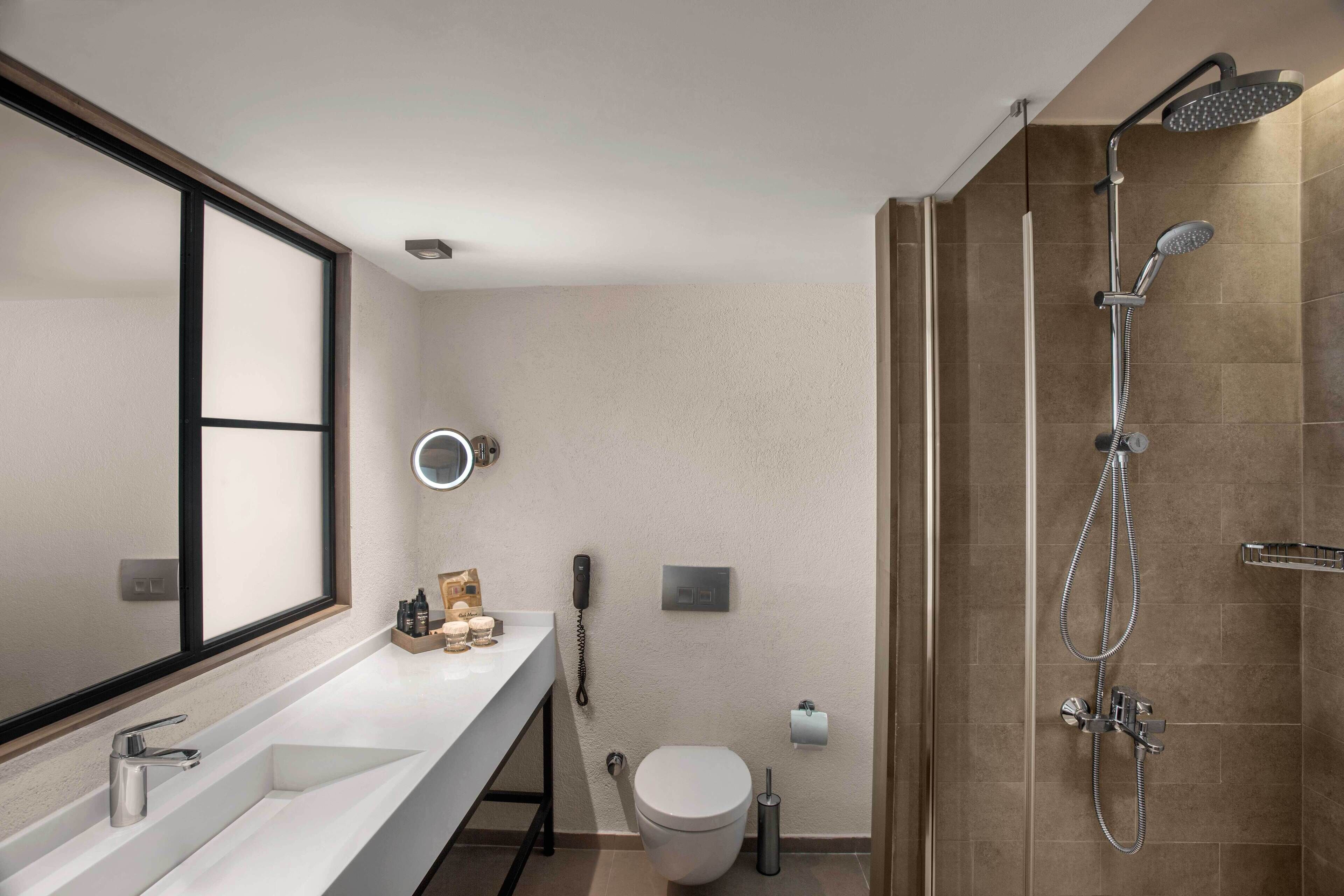 A modern bathroom with a large mirror, a white sink, a toilet, and a shower area.
