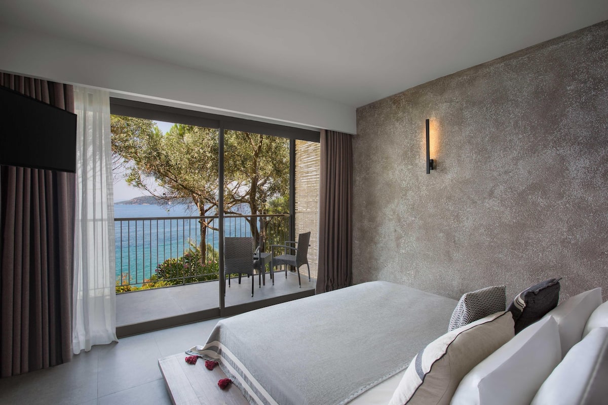 A bedroom with a large window, a bed, a chair, and a table.