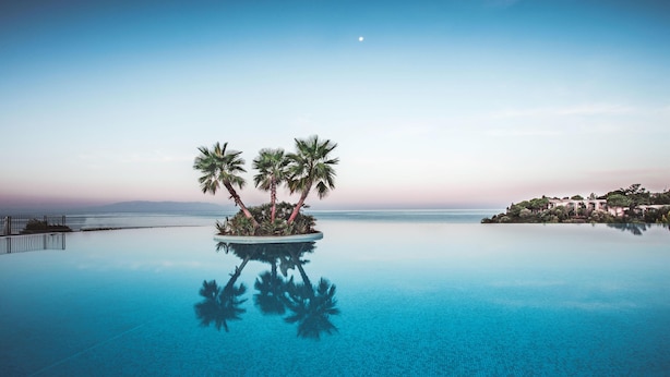 Una piscina infinita de color azul intenso, con palmeras y una luna en el cielo.