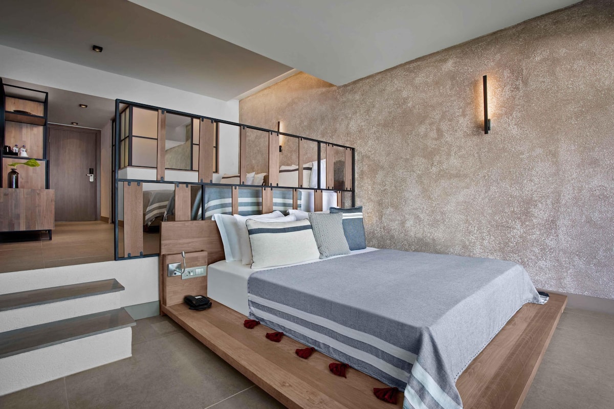 A modern bedroom with a large bed, a wooden platform, and a staircase leading to an upper level.