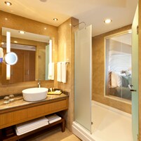 Un baño moderno con un espejo grande, un lavabo redondo y una ducha con cerramiento de vidrio.