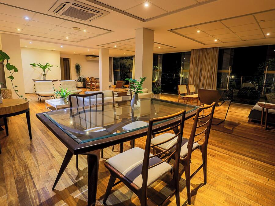 Un comedor moderno con una mesa de vidrio y sillas de madera, rodeado de piso de madera y ventanas amplias.