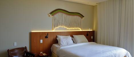 A hotel room with a bed, a wooden headboard, a chair, a small table, and a wall-mounted light fixture.