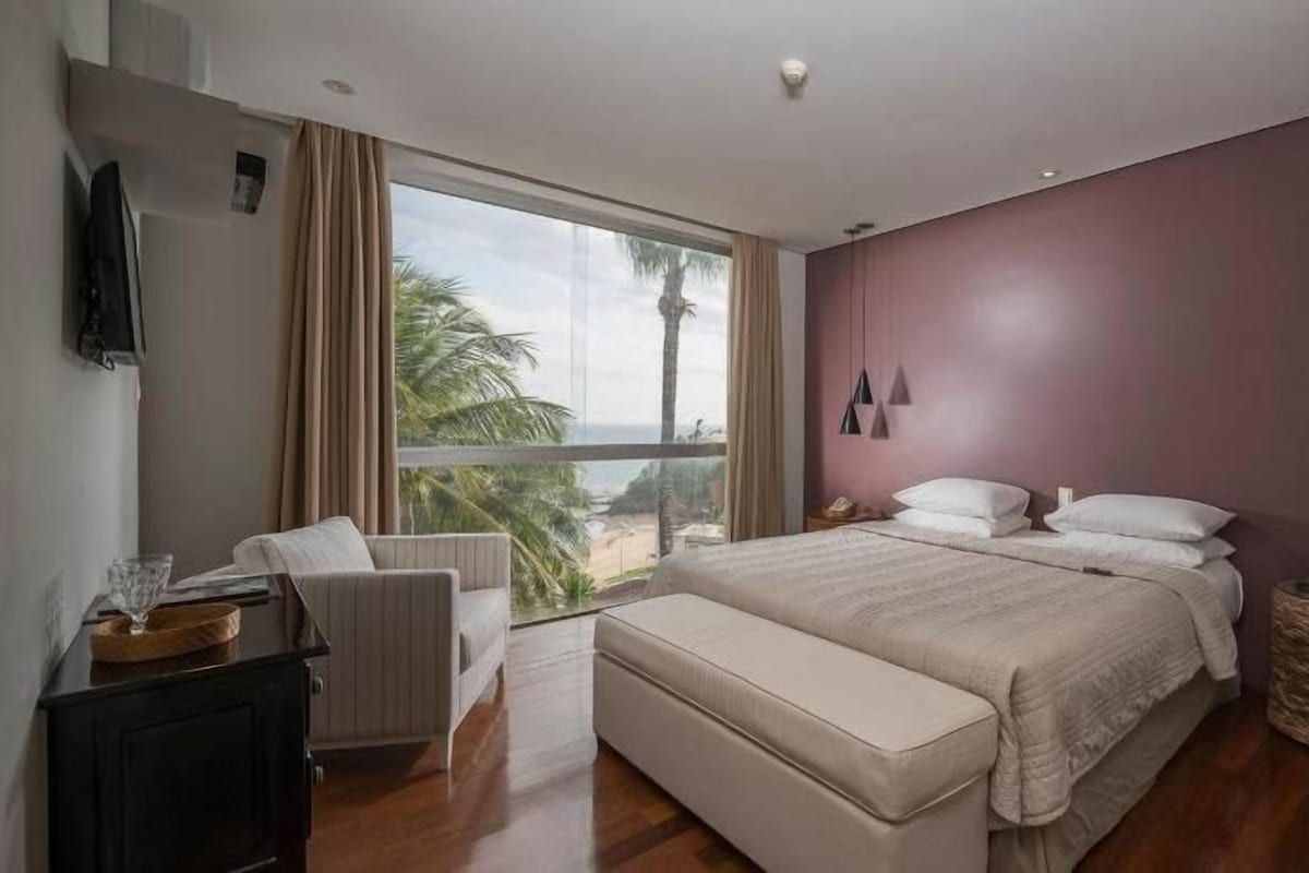 A bedroom with a bed, a chair, a bedside table, and a view of the outdoors.