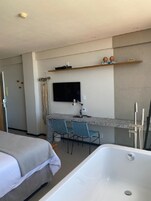 A hotel room with a bed, a desk with two chairs, a TV mounted on the wall, a bathtub, and a shower.