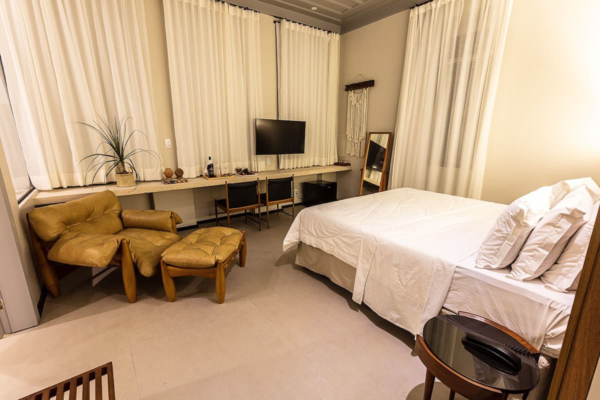 A hotel room with a bed, a desk with a TV, a chair, and a small table with a telephone.
