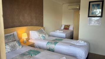 A hotel room with two beds, a nightstand with a lamp, and an air conditioning unit.