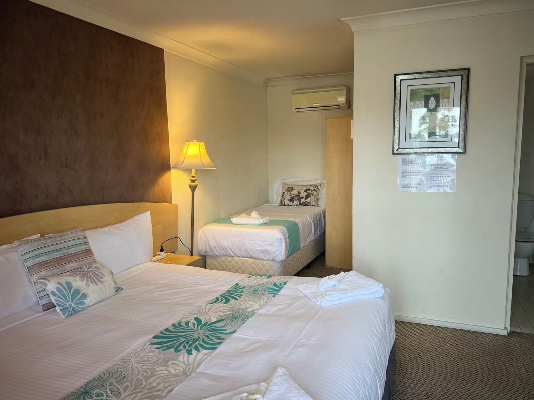 Habitación de hotel con dos camas, una lámpara de noche, un equipo de aire acondicionado y un cuadro en la pared.