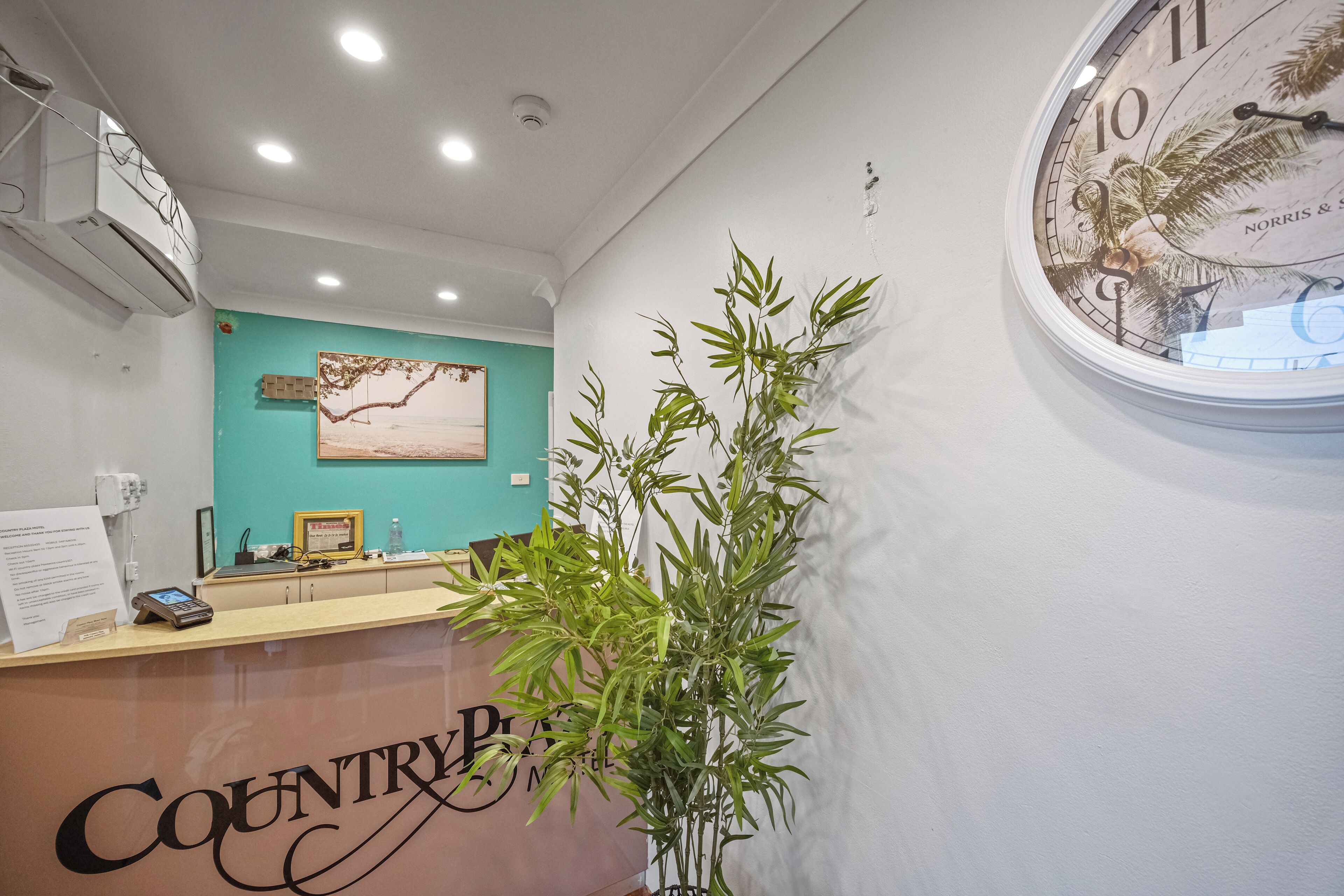Mostrador de recepción con un reloj, una planta y una pared color aguamarina.