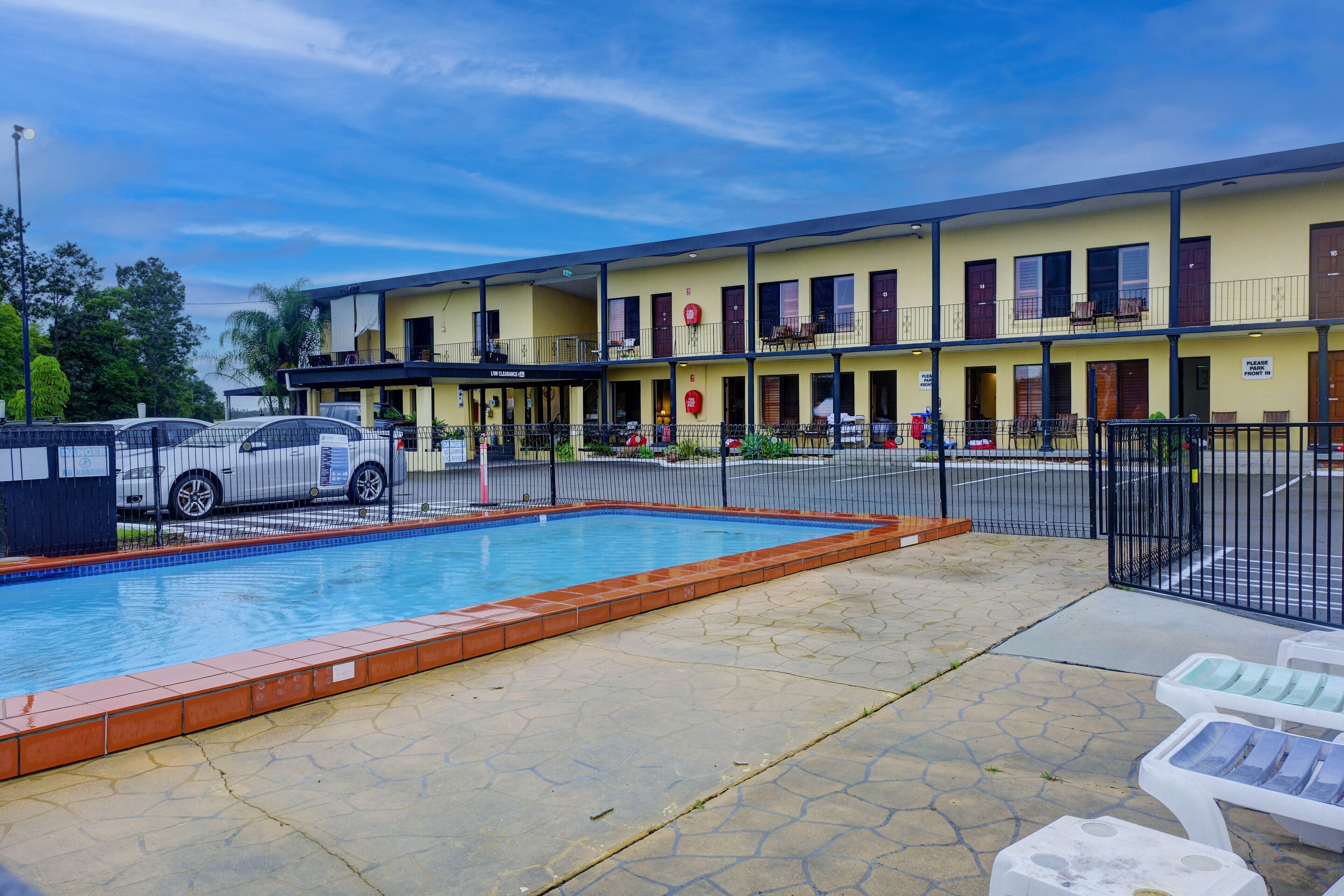 A hotel with a swimming pool, outdoor seating, and a fenced parking area.