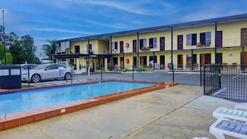 A hotel with a swimming pool, outdoor seating, and a fenced parking area.