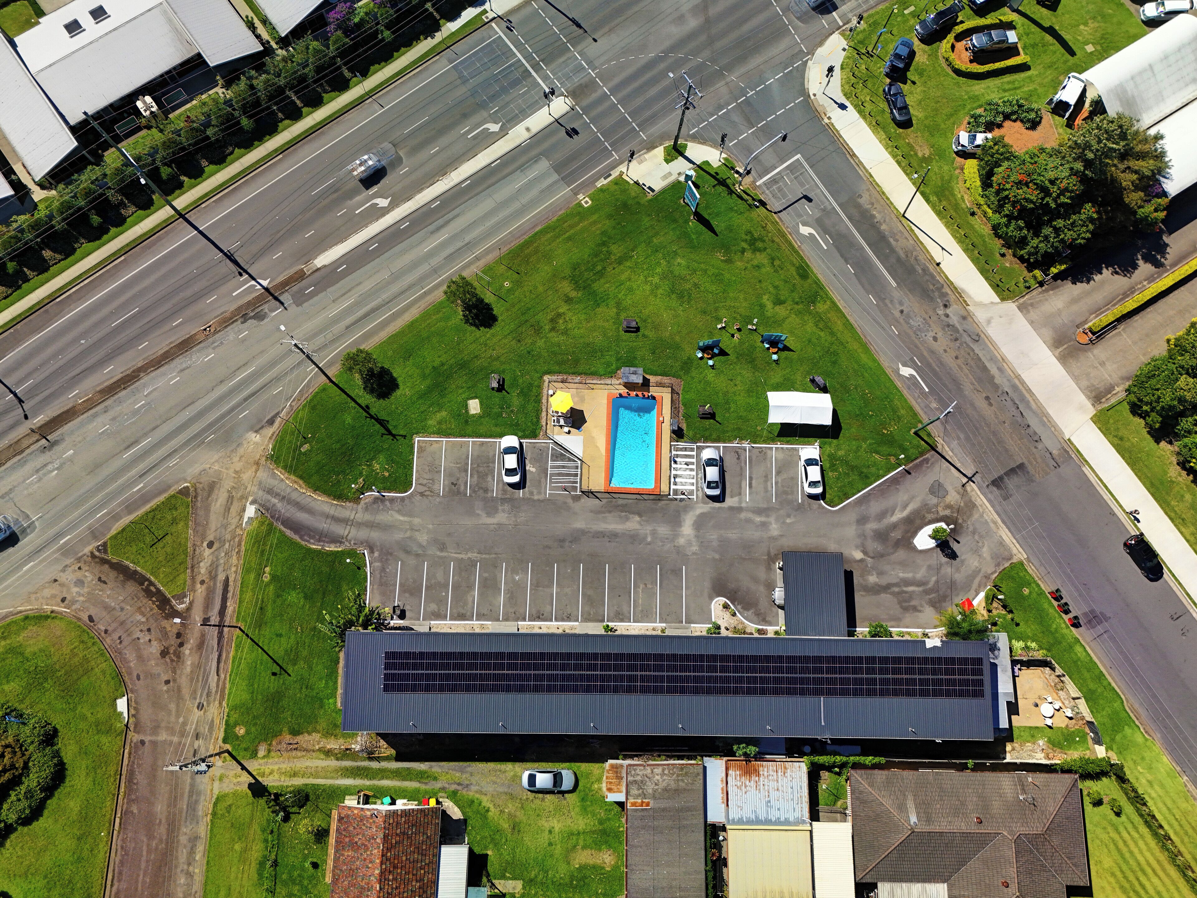 An aerial view of a parking lot with a swimming pool, a covered area, and a building with a flat roof.