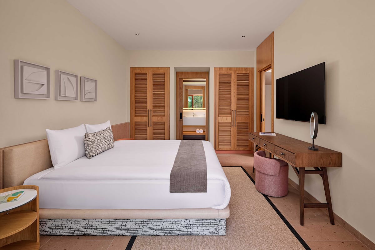 Een moderne hotelkamer met een groot bed, een houten kledingkast, een bureau met spiegel en een flatscreen-televisie.