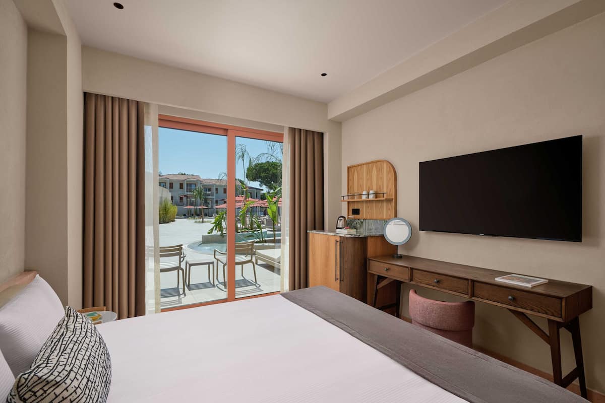 Hotelkamer met een groot bed, een bureau met spiegel, een flatscreen televisie en uitzicht op een binnenplaats met terras en zwembad.