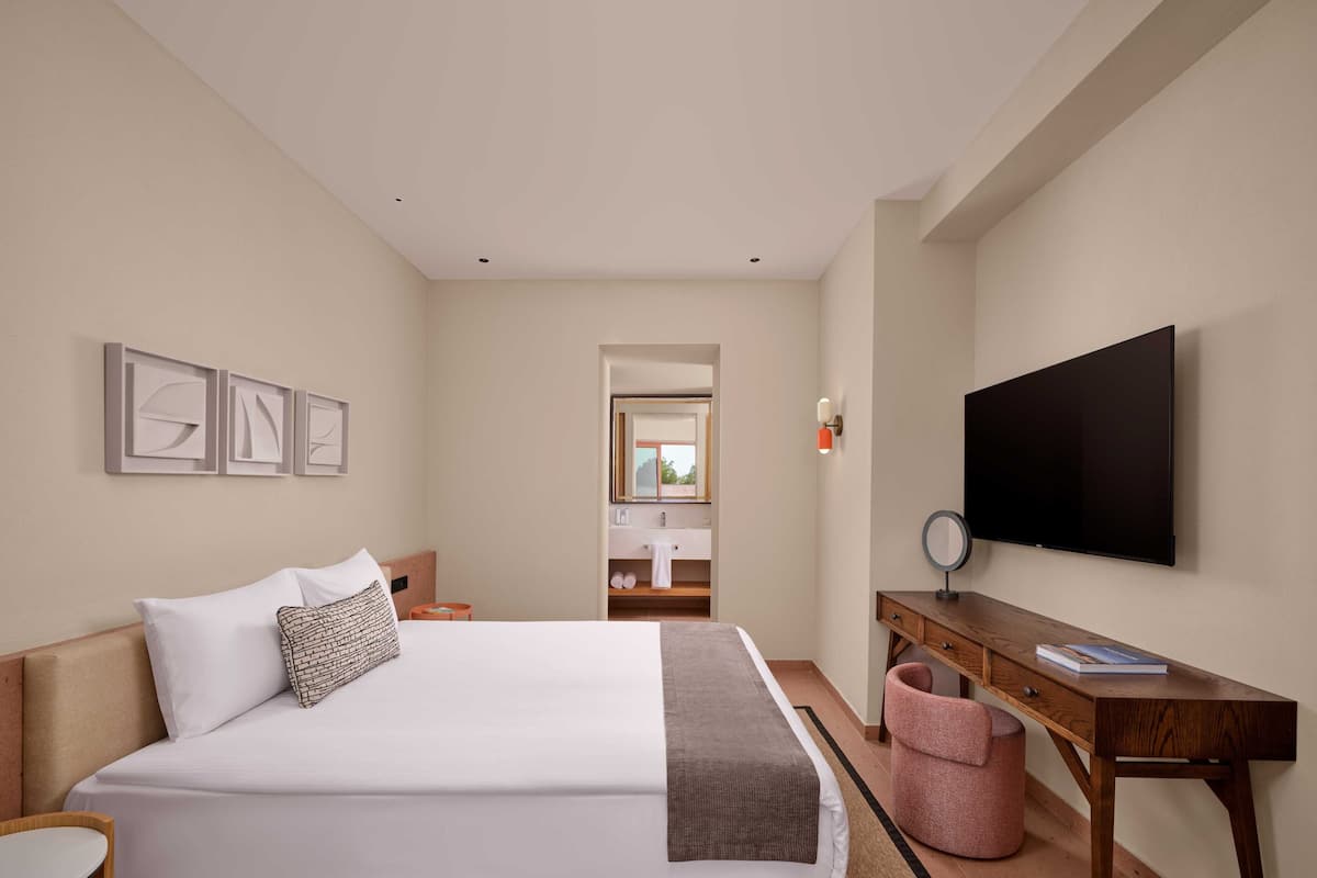 Een hotelkamer met een groot bed, een bureau, een televisie en een spiegel.