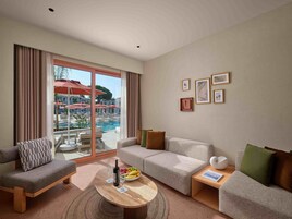 Ein modernes Hotelzimmer mit Blick auf einen Pool, zwei Sofas, einem Couchtisch mit einer Flasche und Gläsern sowie gerahmten Bildern an der Wand.