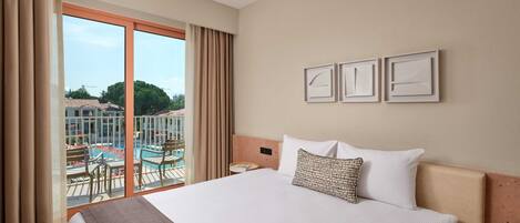 A hotel room with a large bed, a view of a pool and outdoor area, and three framed pictures on the wall.