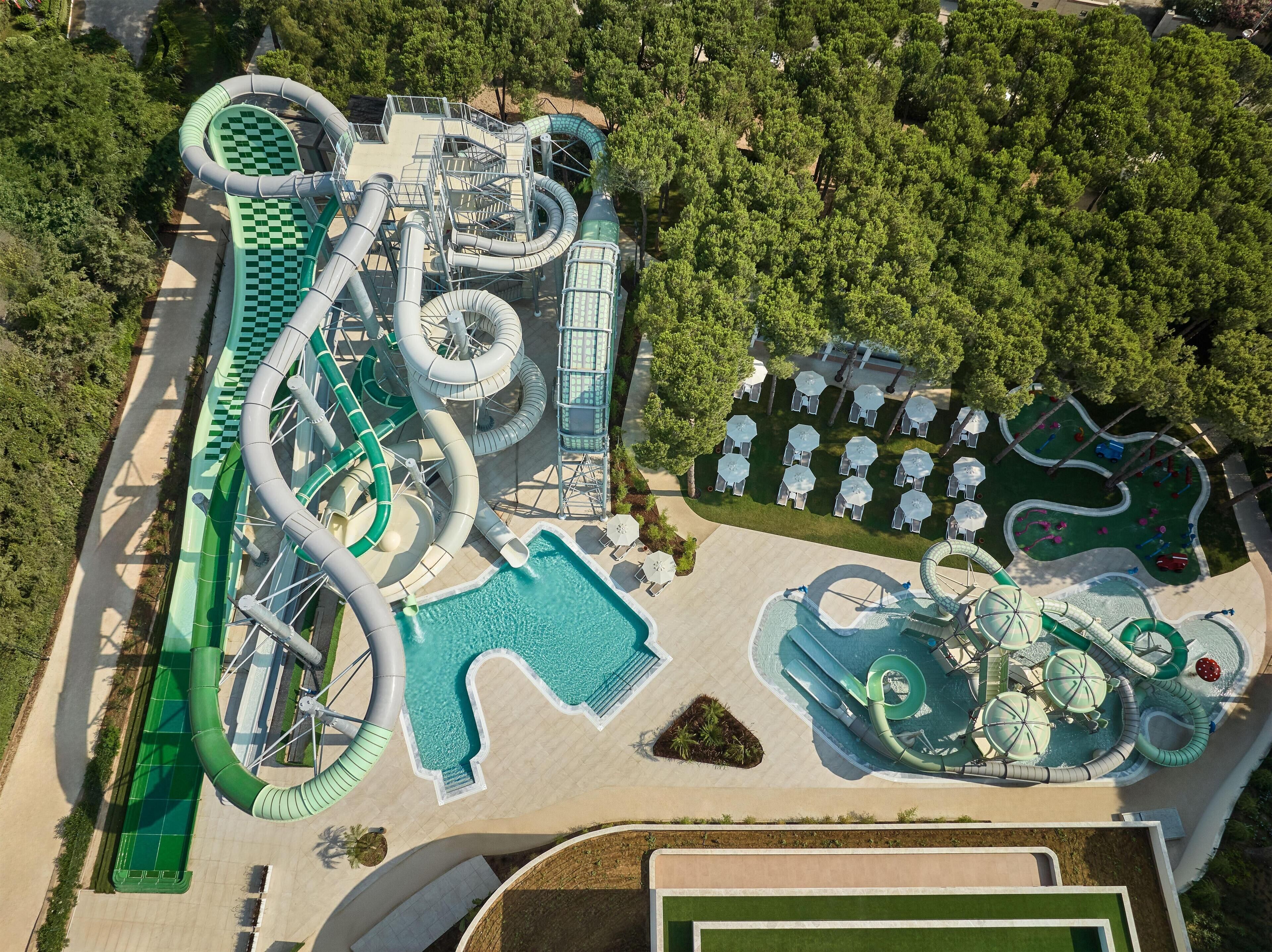 Luchtbeeld van een waterpark met meerdere glijbanen en zwembaden, omgeven door bomen en terrassen.